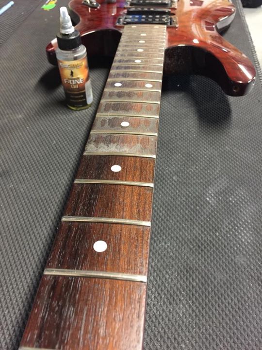 MUSIC NOMAD MN105 FRETBOARD OIL CLEANER AND CONDITIONER DEMO PHOTO F-ONE BOTTLE ON WORKBENCH BY RED ELECTRIC GUITAR WITH OILED VS UN OILED FRETS