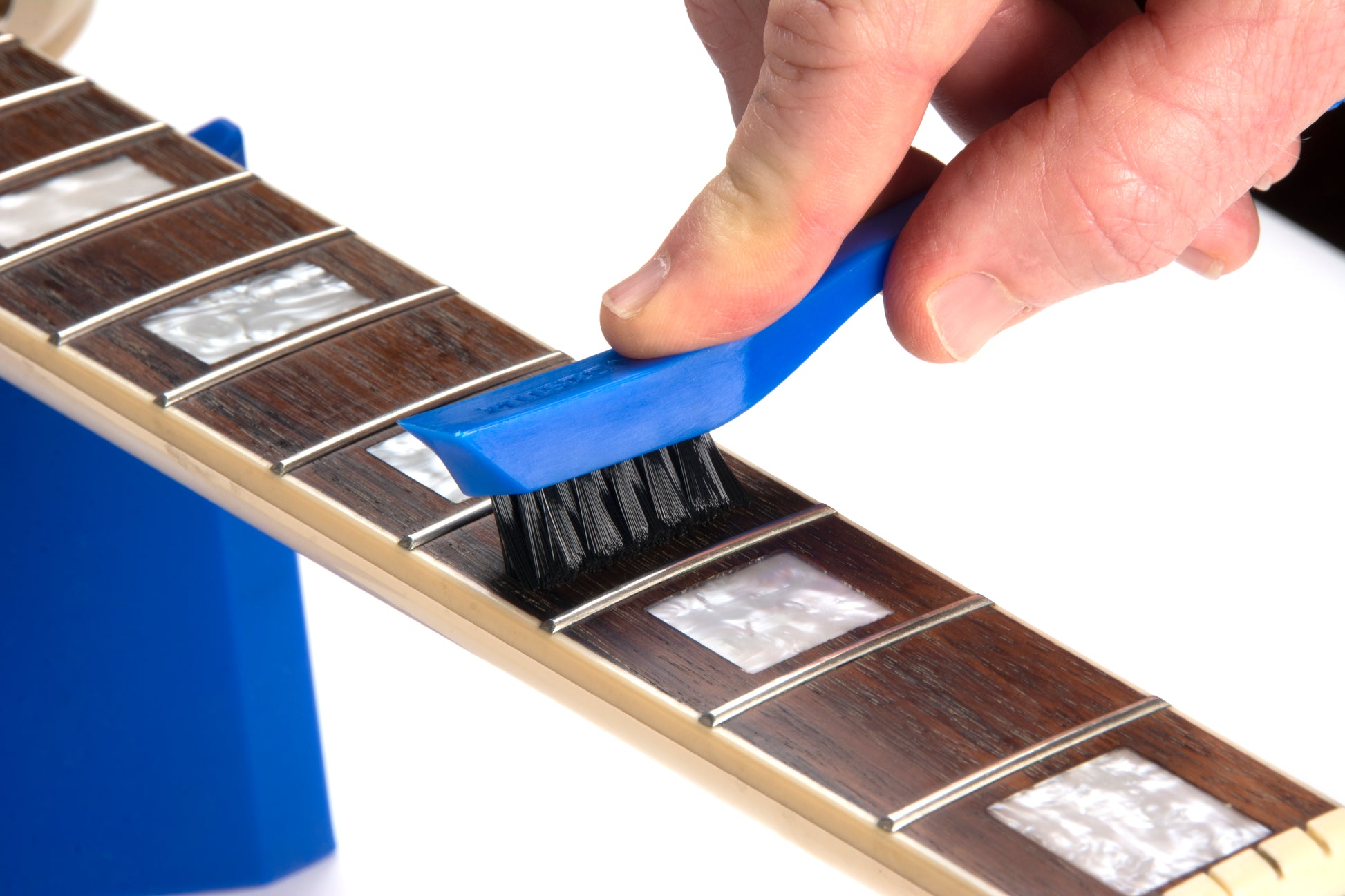 MUSIC NOMAD MN125 UNINISHED FRETBOARD CARE KIT DEMO PHOTO HAND USING FRETBOARD CLEANING BRUSH ON WHITE BACKGROUND