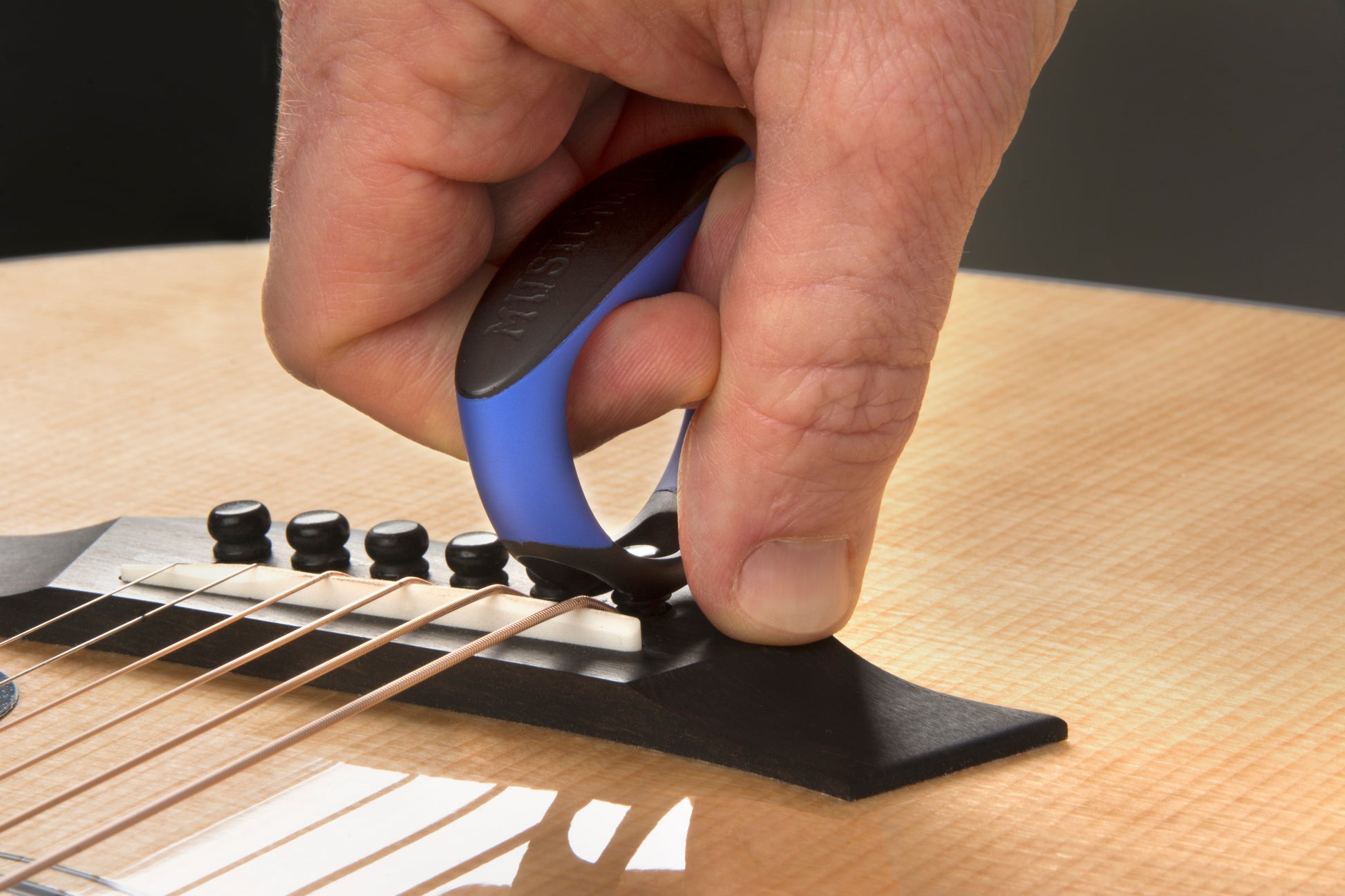 MUSIC NOMAD MN219 GRIP PULLER CLOSEUP OF HAND PULLING BRIDGE PIN ON ACOUSTIC GUITAR
