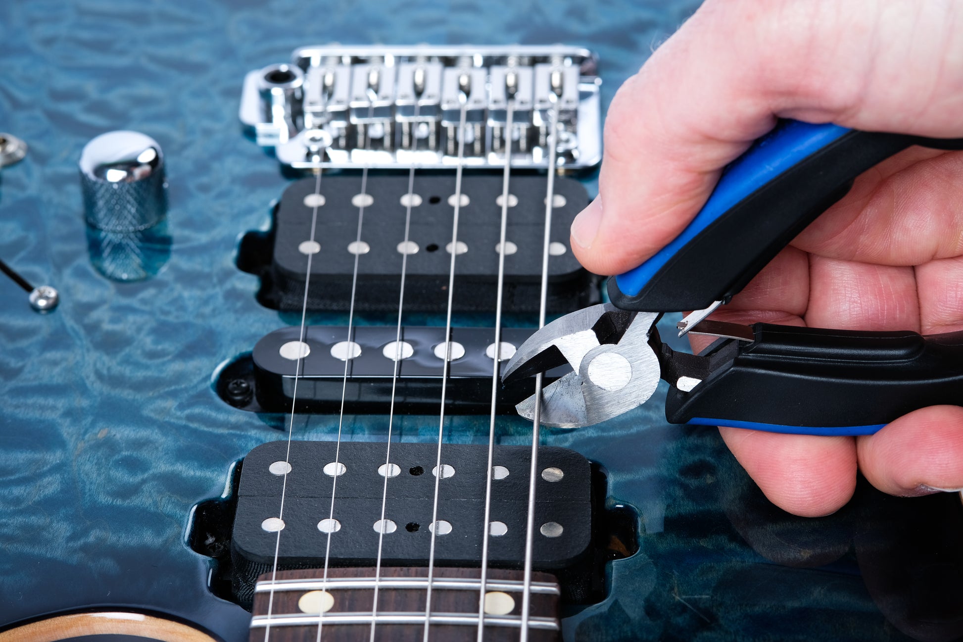 MUSIC NOMAD MN226 MUSICNOMAD GRIP CUTTER CLOSEUP DEMO HAND CUTTING E STRING ON BLUE ELECTRIC GUITAR