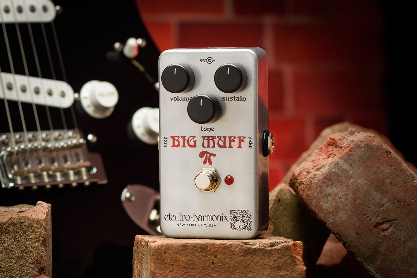 ELECTRO-HARMONIX EHX RAM'S HEAD BIG MUFF PI  PROMO PIC ON BRICK WITH GUITAR AND RED BRICK IN BACKGROUND