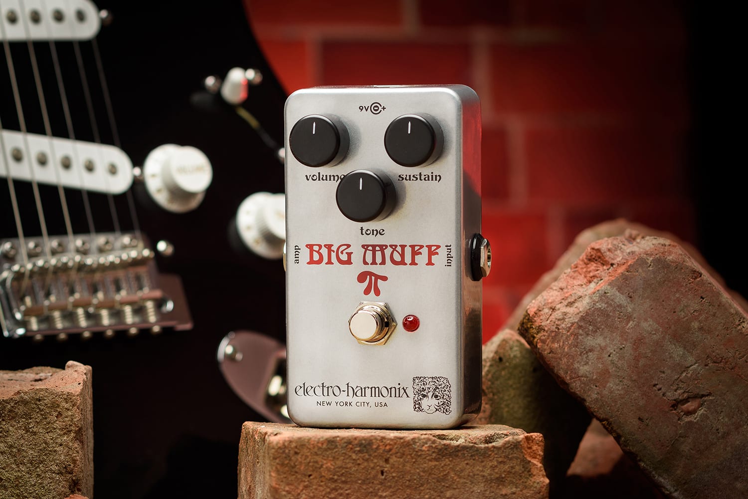 ELECTRO-HARMONIX EHX RAM'S HEAD BIG MUFF PI  PROMO PIC ON BRICK WITH GUITAR AND RED BRICK IN BACKGROUND